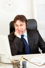 Smiling  businessman with headset looking at monitor.