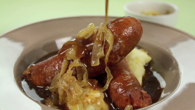 Pouring gravy and putting basil on bangers and mash