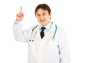 Fototapeta na wymiar Smiling young medical doctor pointing finger up