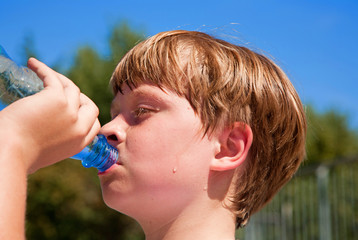 young boy drinks water out of a bottle after sports