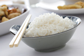 A bowl of white rice with some dishes in the background