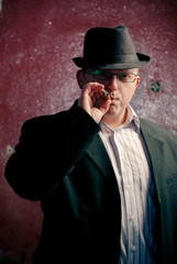 Fototapeta na wymiar man in black suite on red wall with sigare. Gangster theme
