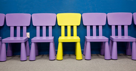 A yellow colored one in the middle of purple colored chairs