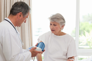 Fototapeta premium Mature doctor taking the blood pressure of his patient