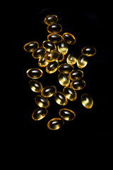 Cod liver oil capsule pills on a black studio background.