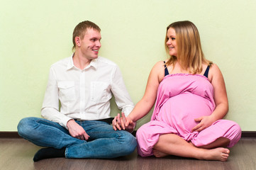 Fototapeta na wymiar Pregnant woman with her husband sitting on floor in empty room
