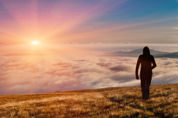 silhouette of the man walking above the clouds on the sunrise