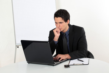 Junger Mann erfolgreich nachdenklich am Laptop