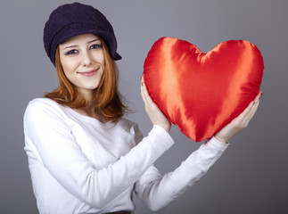 Beautiful red-haired girl in cap with toy heart.
