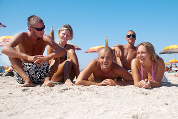 Portrait of happy girls and guys lying on sand on summer vacatio