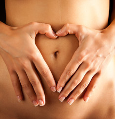 Woman touches tummy forming a heart shape with her fingers.