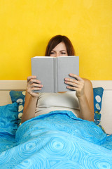 young woman sitting on bed and reading book, bright interior