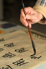 An old man is practicing callingraphy using a brush pen