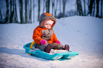 Fototapeta na wymiar Serious cute baby sliding on sleigh from hill in park