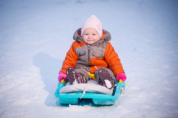 Fototapeta na wymiar Adorable baby sliding on sleigh from hill in park and smile