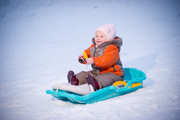 Adorable baby sliding on sleigh from hill in park and smile