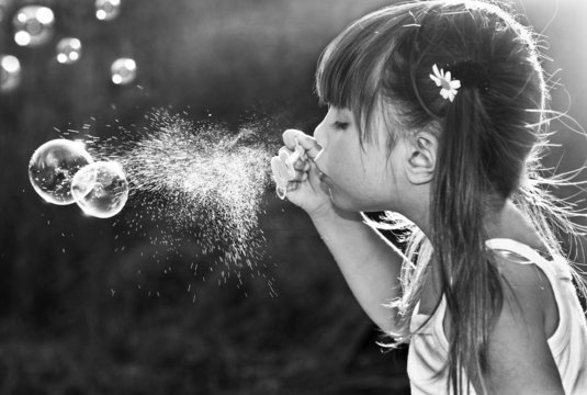 Black and white portrait of a little girl blowing soap bubbles