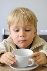 Little boy drinks tea and watch the cup