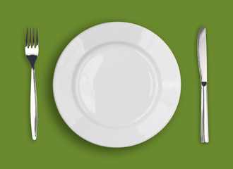Knife, white plate and fork on green background