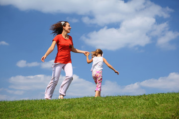 Mother with daughter hurry and play on  grass in  day-time