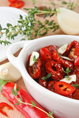 Marinated dried tomatoes, garlic, thyme, in a white bowl.