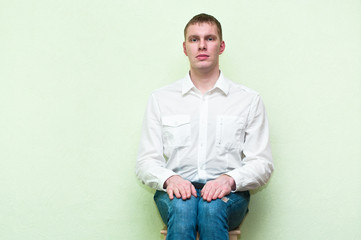 Handsome young man sitting near the wall. Copy space