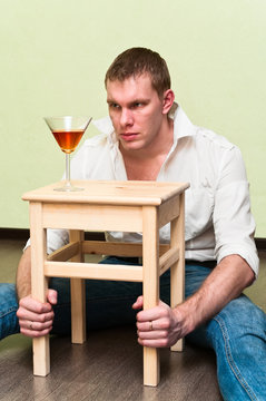 Man sitting on floor with glass of alcohol and looking at it