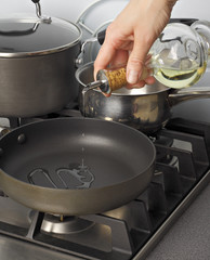 Cooking oil being pourred from a glass bottle into a frying-pan.
