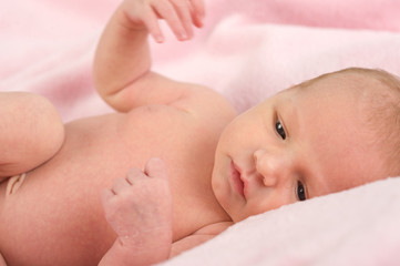 Neugeborenes liegt auf rosa Decke und schaut