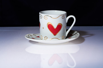 White cup with hearts stands on a white table.