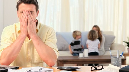 Man calculating his bills with his family in the background - Powered by Adobe