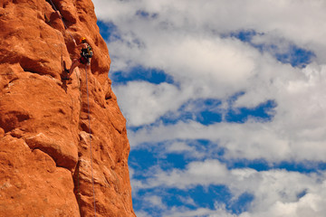 Climber on red rock against blue sky and white clouds