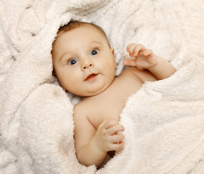 The baby lies in a white towel. He smiles