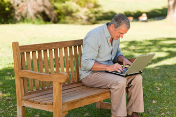Fototapeta premium Elderly man working on his laptop in the park