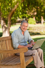 Fototapeta premium Elderly man working on his laptop in the park