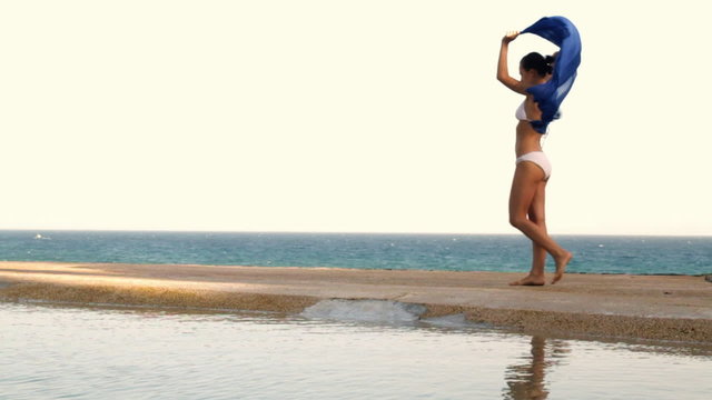 Woman with waving sarong walking on the seashore, slow motion