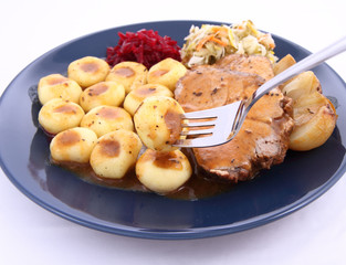 Pork steak and dumplings with salads being eaten with a fork