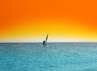 Fototapeta premium surfer on blue sea under orange sky