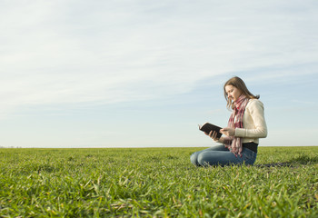 Naklejka na ściany i meble Girl reading a book sitting at grass