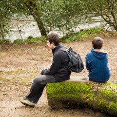 two brothers sitting on a mossy log by riverside