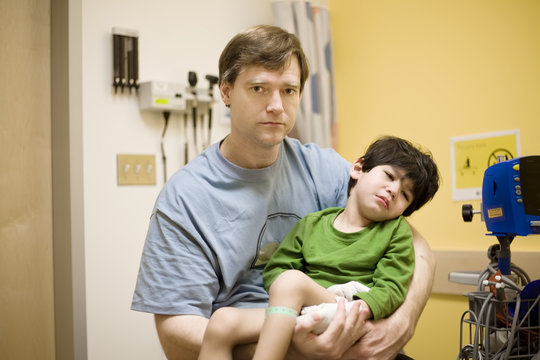 Worried father holding his sick disabled son in doctor's office