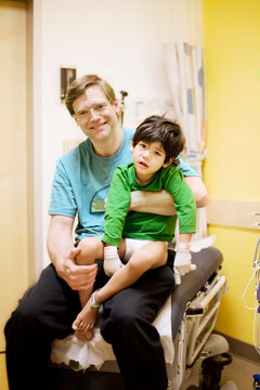 Father holding his sick disabled son in doctor's office