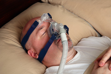 Naklejka premium Man with sleep apnea using a CPAP machine in bed.