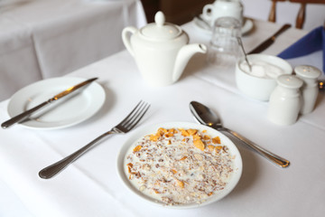muesli in bowl of milk on table with white tablecloth, breakfast