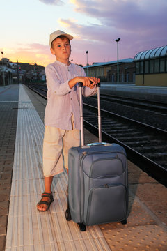 little boy stands on platform of railway with  travel bag