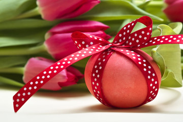 Osterei mit gepunkteter roter Schleife vor Tulpen