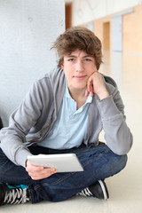 School boy with electronic tablet sitting in hall