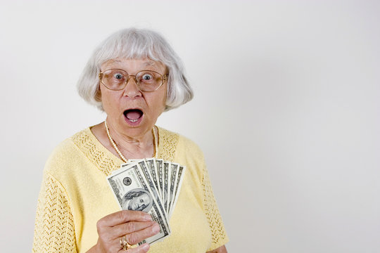 Shocked senior woman holding lots of cash