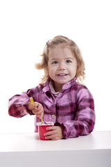 smiling little girl eating youghurt. isolated on white