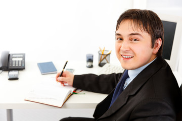 Smiling modern businessman planning timetable in diary.